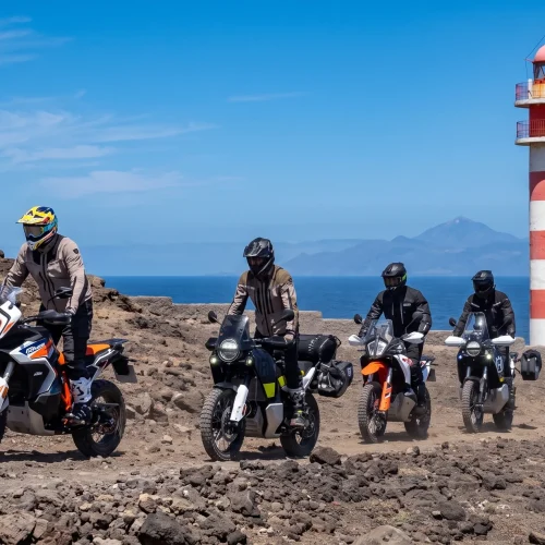 Riders on adventure motorcycles passing a red and white lighthouse on the Canary Islands tour