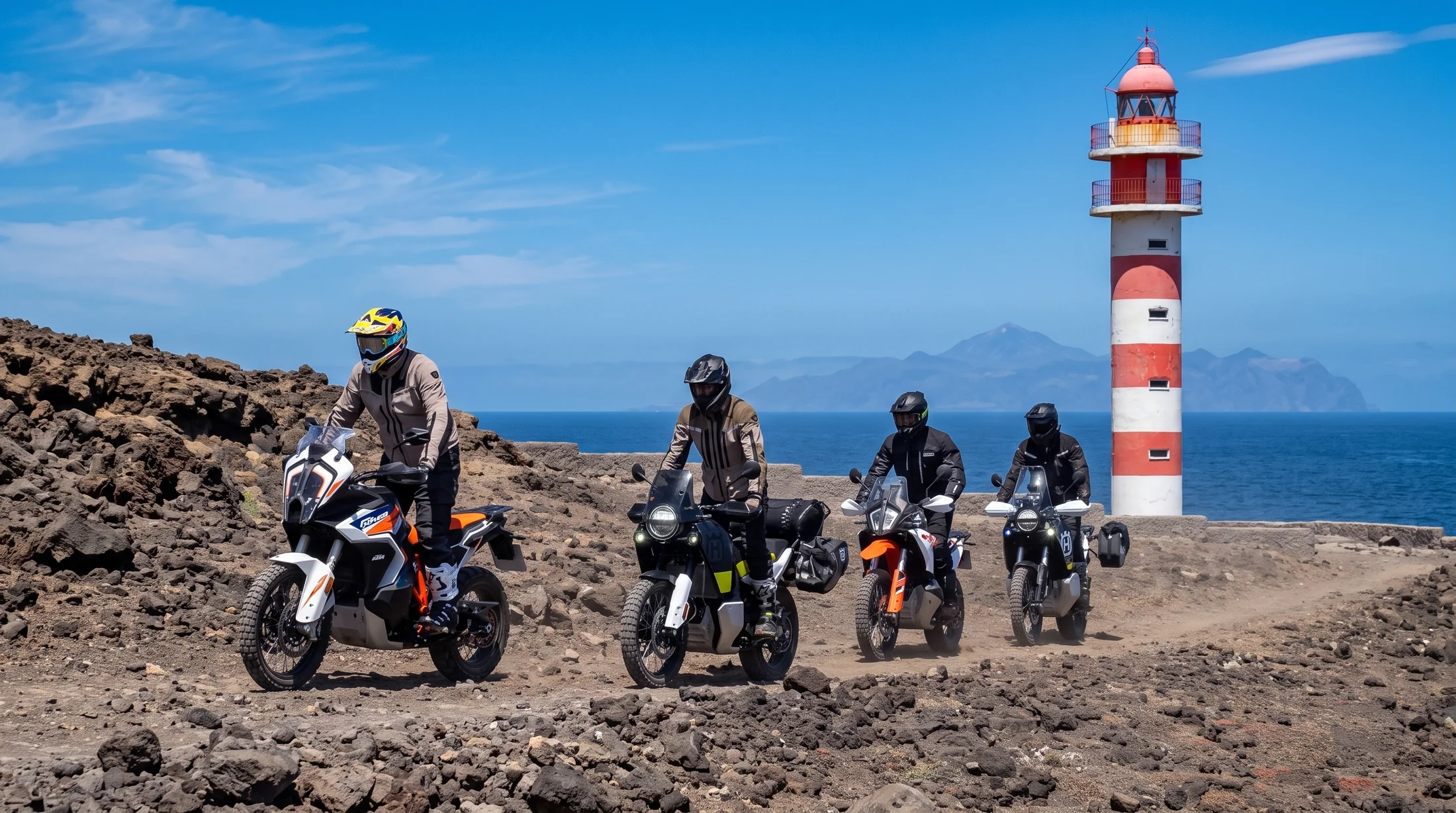 Riders on adventure motorcycles passing a red and white lighthouse on the Canary Islands tour