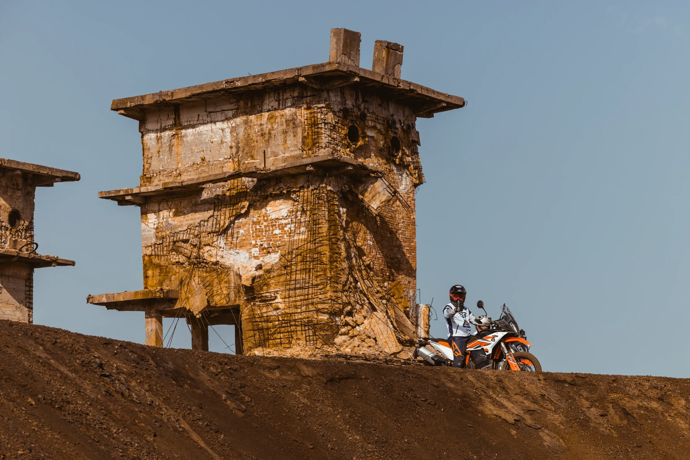 Rider on a KTM adventure bike below an abandoned stone ruin on a hilltop