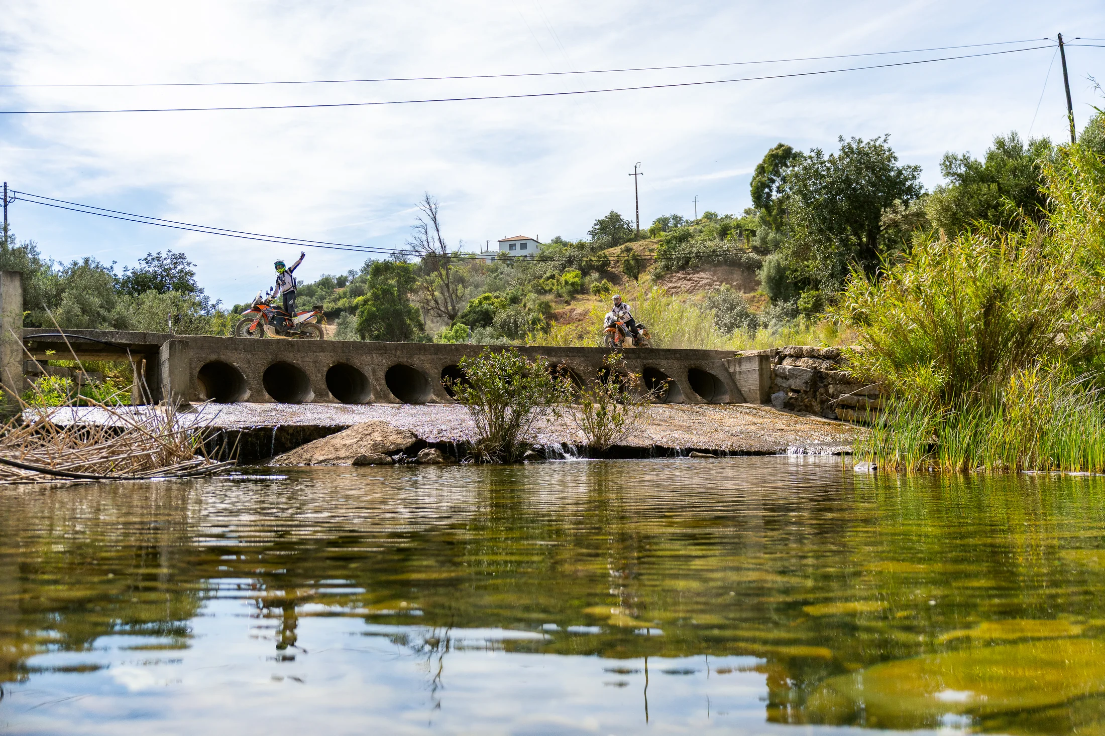 Riders crossing a low concrete bridge over a river in Portugal