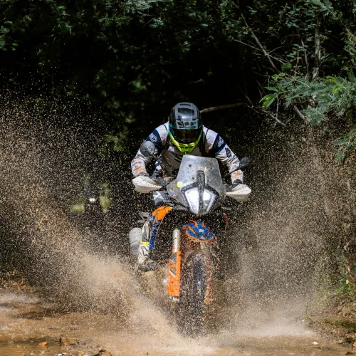 Rider on a KTM adventure bike splashing through a muddy forest track on the 6 Days Portugal ISDE tour