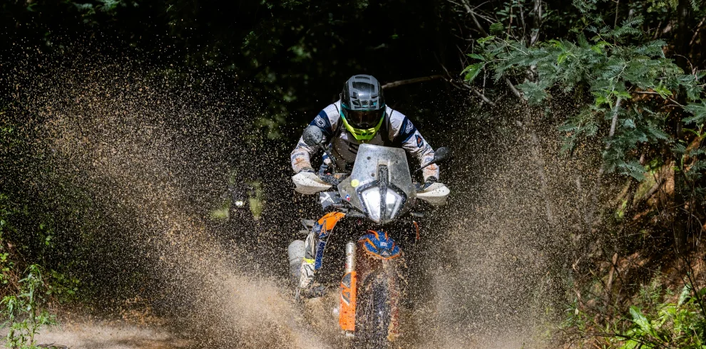 Rider on a KTM adventure bike splashing through a muddy forest track on the 6 Days Portugal ISDE tour