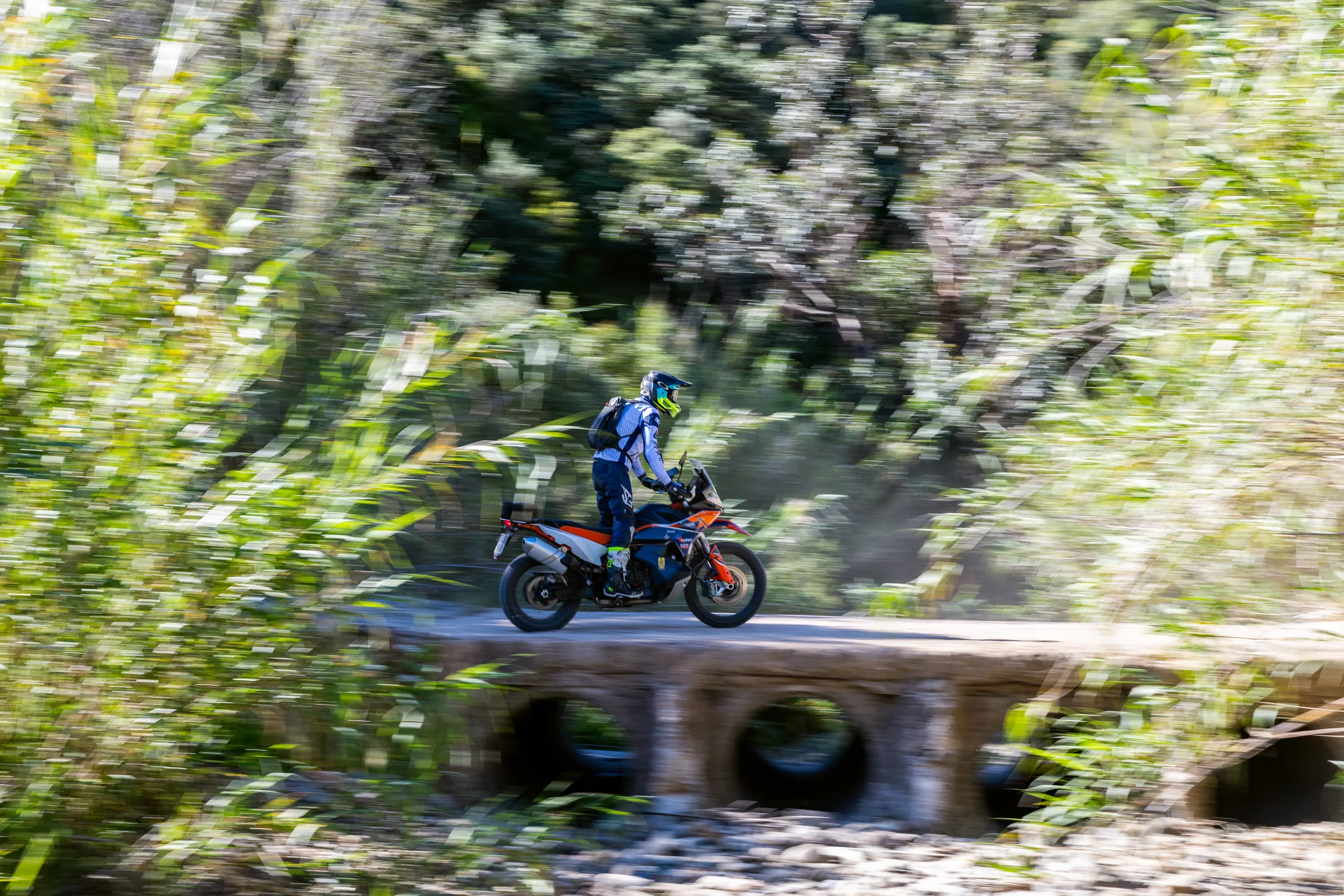 Rider on a KTM adventure bike crossing a low stone bridge