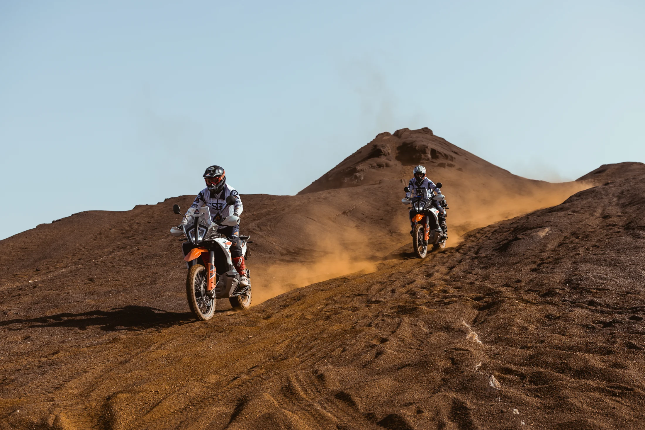 Two riders on KTM adventure bikes riding over red earth mounds at an old mine