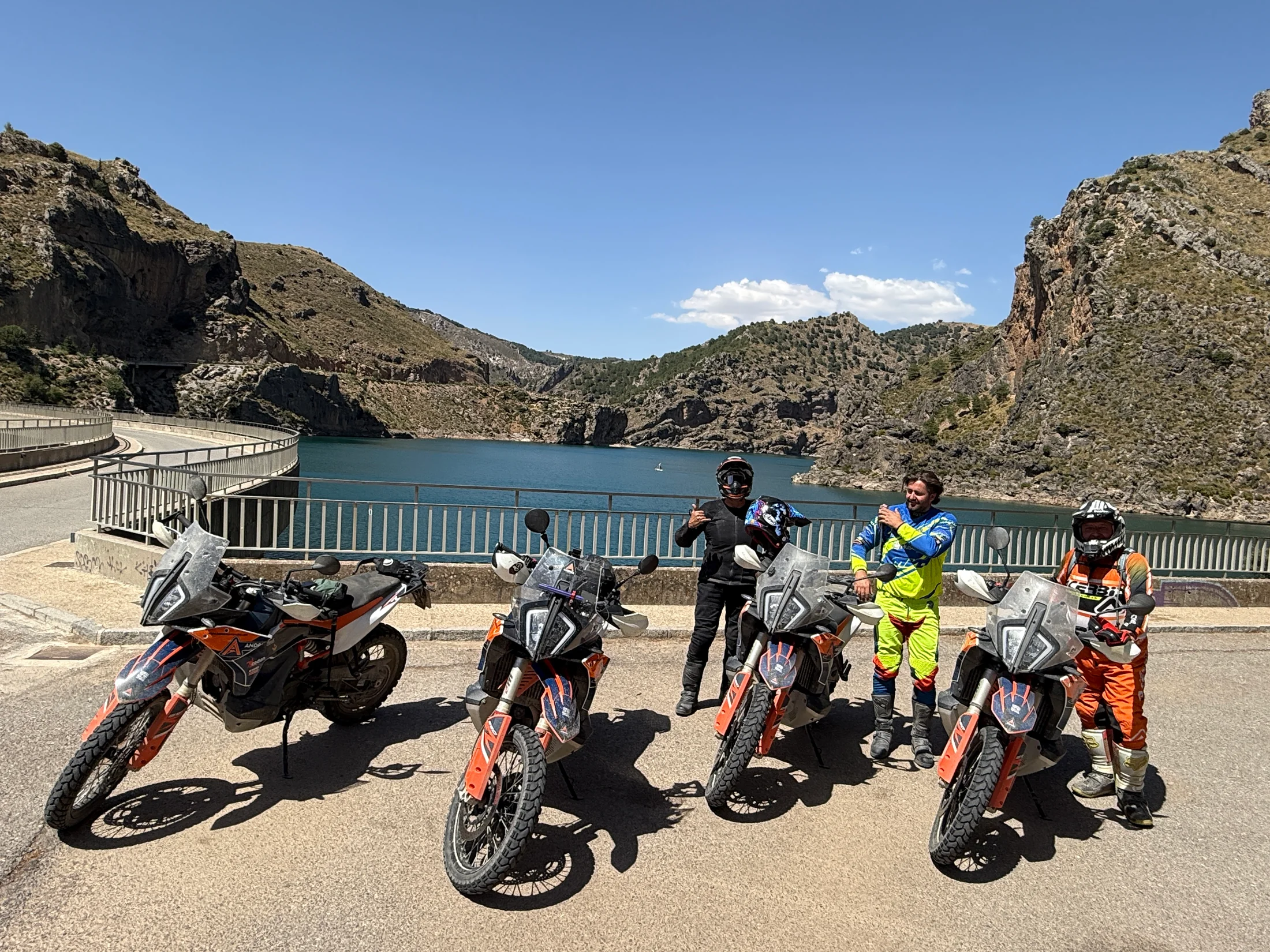 Riders posing with their KTM adventure bikes on a dam above a mountain reservoir in Andalusia