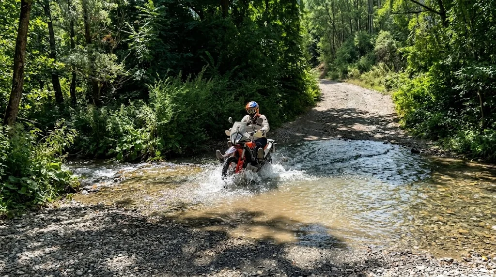 Rider on a KTM adventure bike crossing a shallow ford on a forest track
