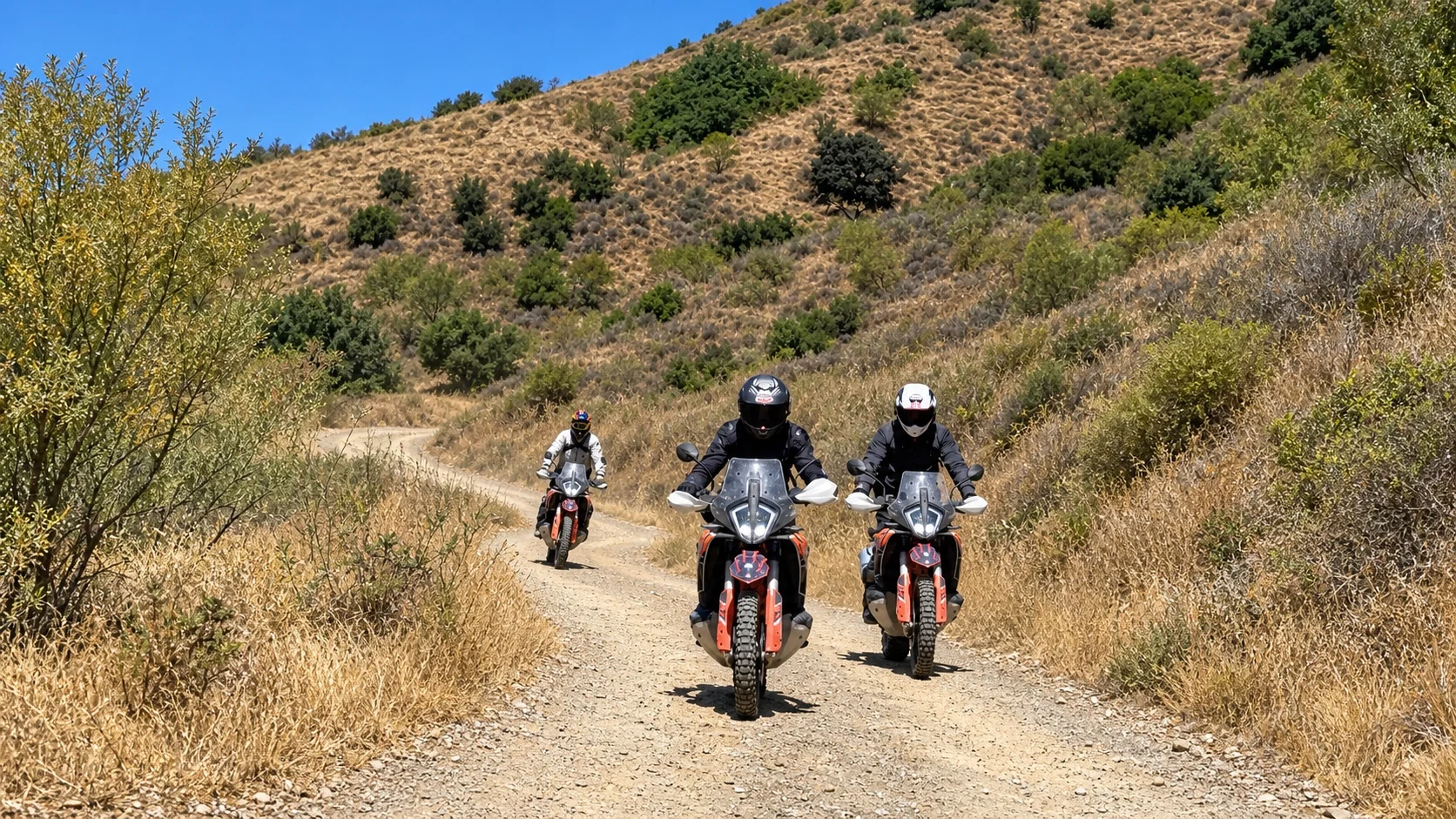 Three riders on KTM adventure bikes on a dirt track through dry Andalusian hills
